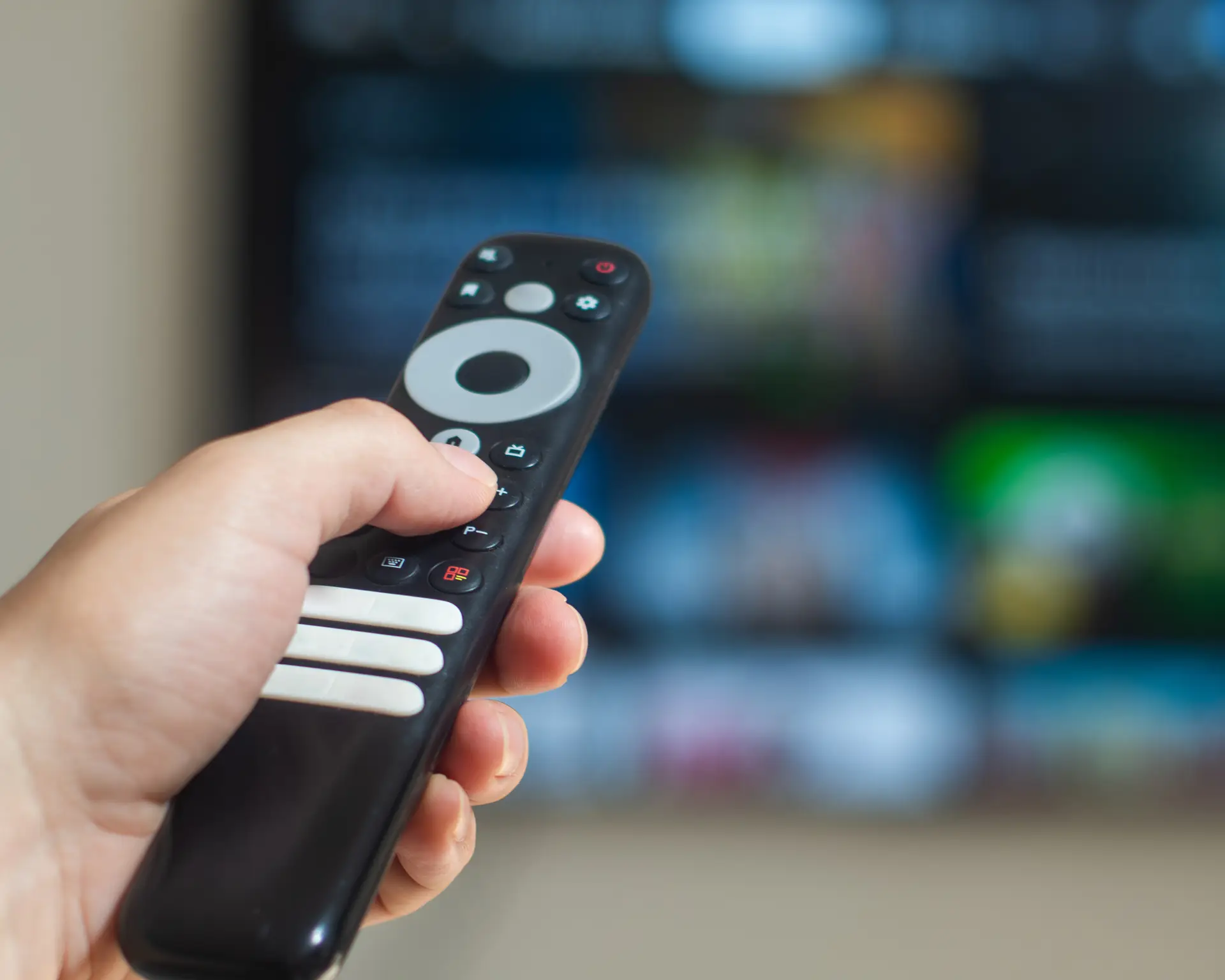 Hand holding a TV remote pointed at a television screen.