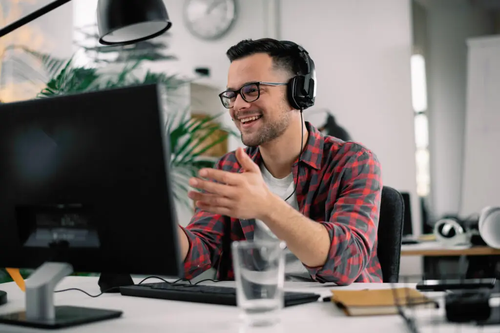 Person wearing a headset and smiling while participating in a video call at a desk.