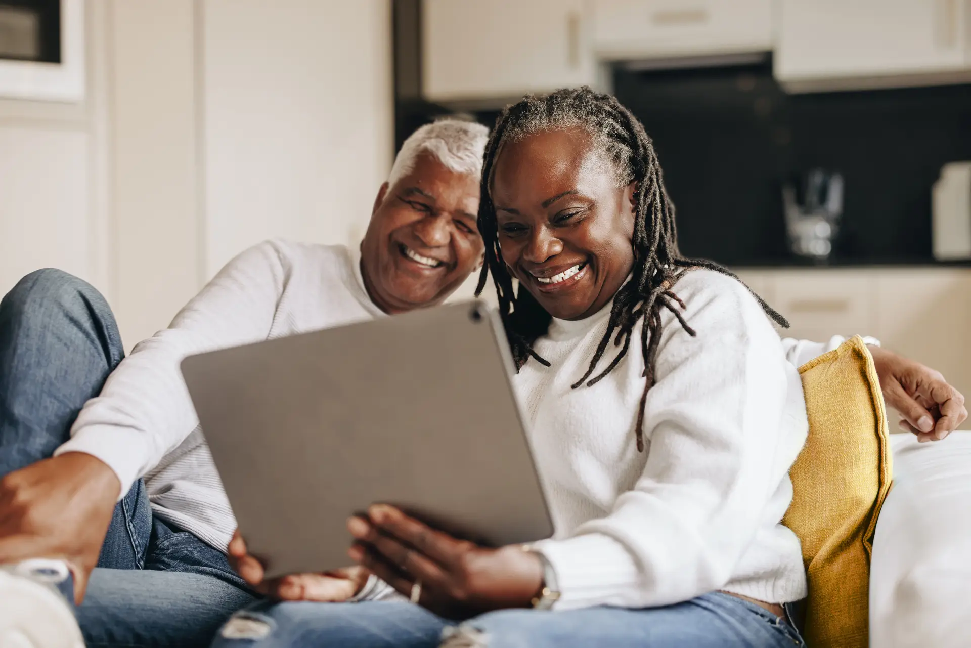 Smiling couple sitting on a couch, looking at a tablet together.