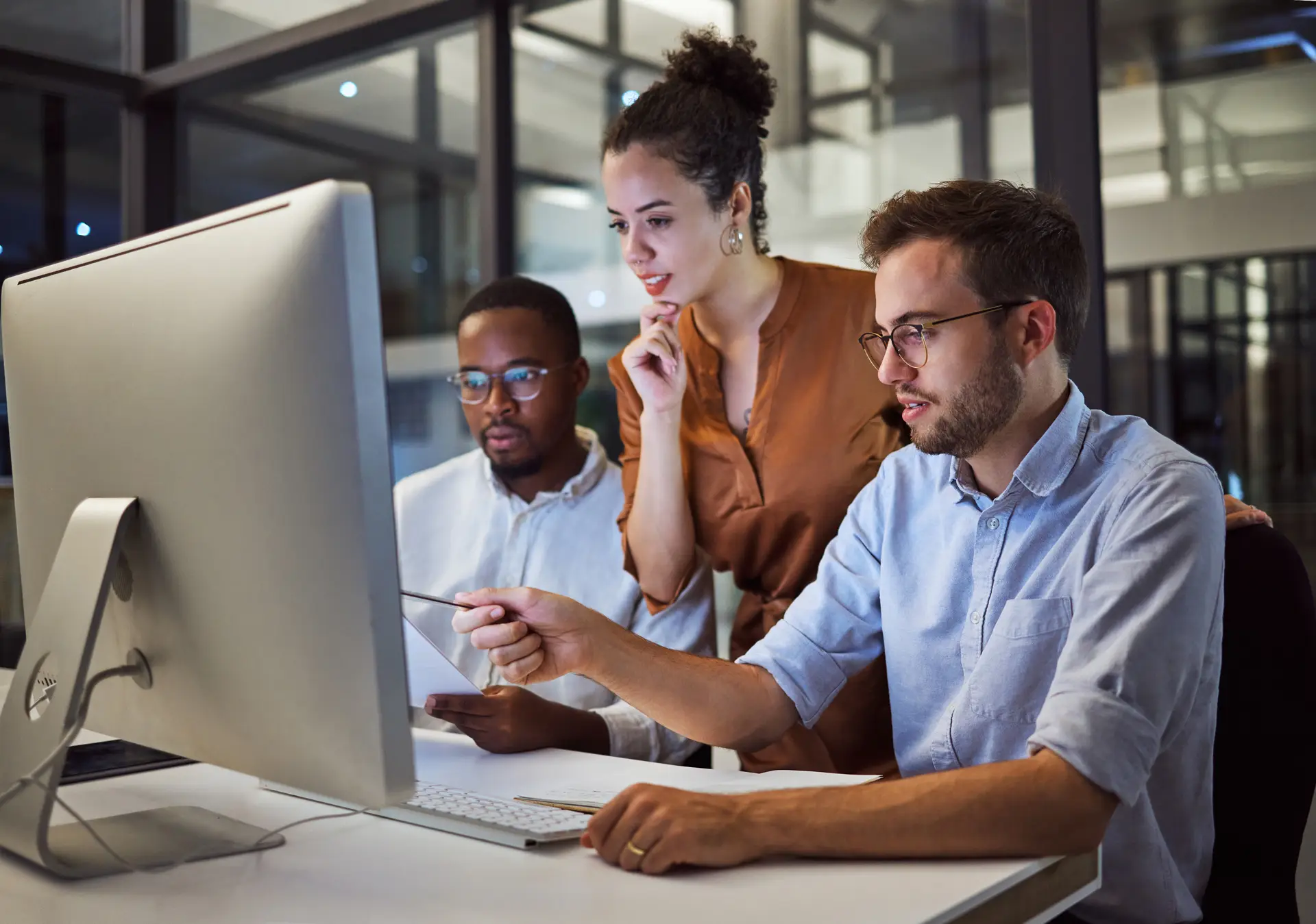 Three coworkers collaborating at a desktop computer in a modern office.