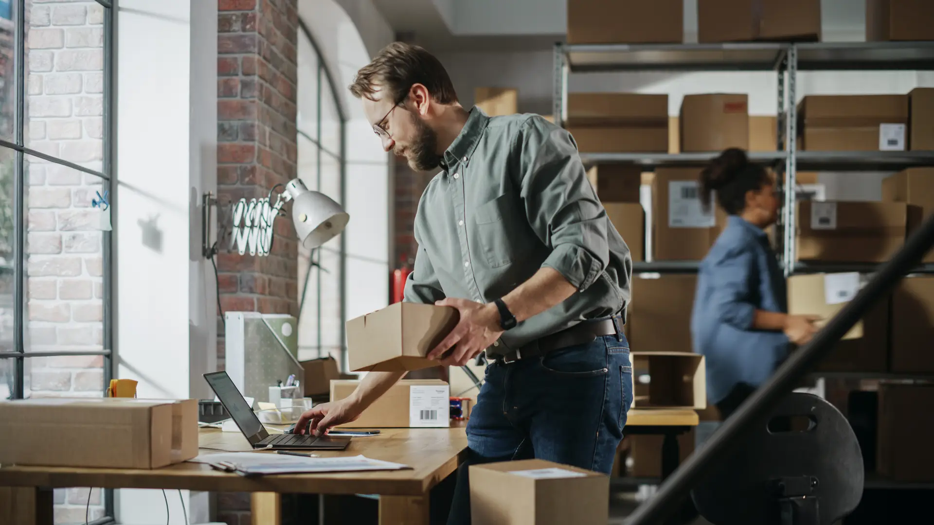 Warehouse worker scanning a package while using a laptop in a shipping and fulfillment workspace.