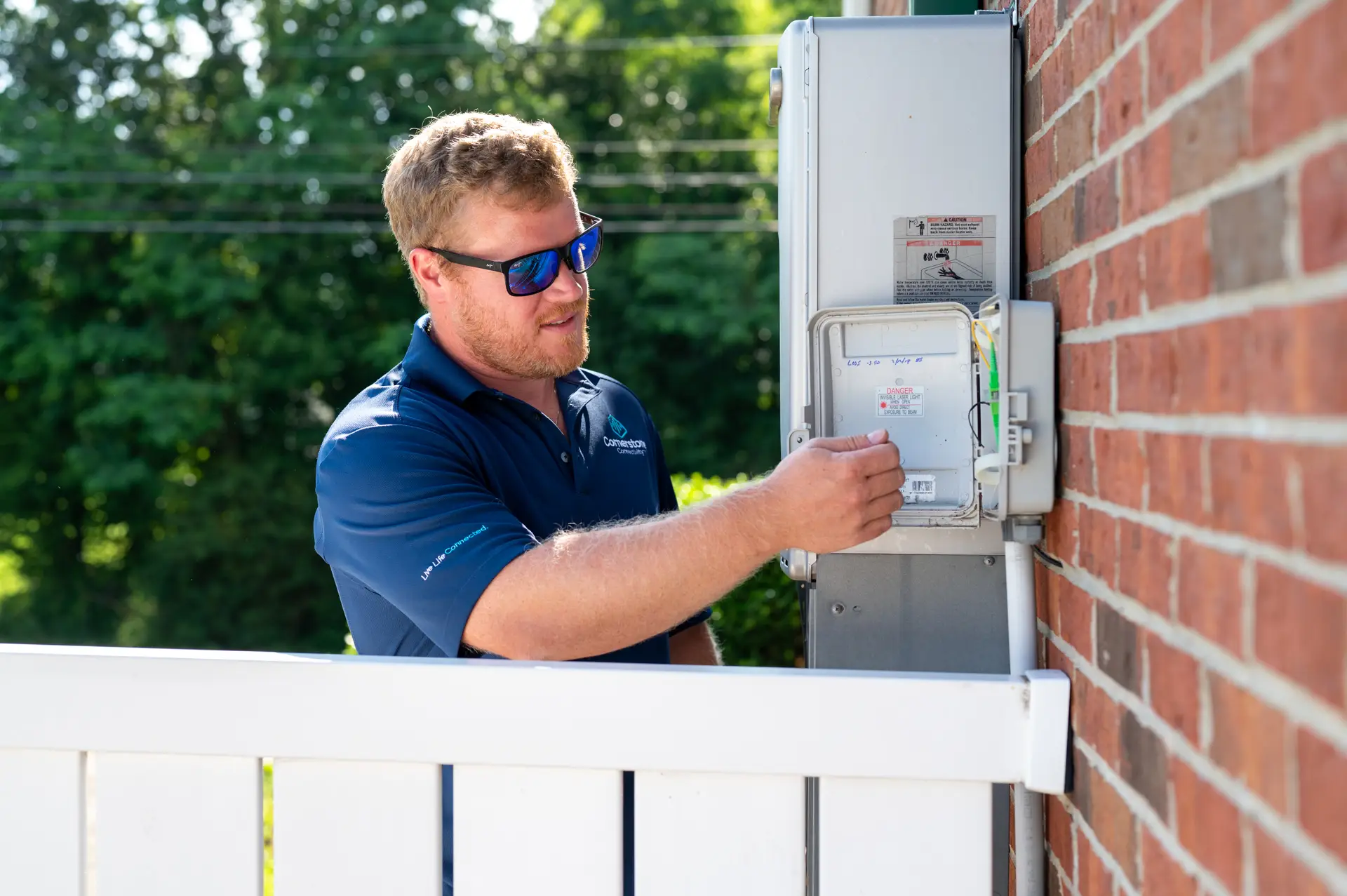 Cornerstone Connectivity technician servicing an outdoor utility box mounted on a brick wall.