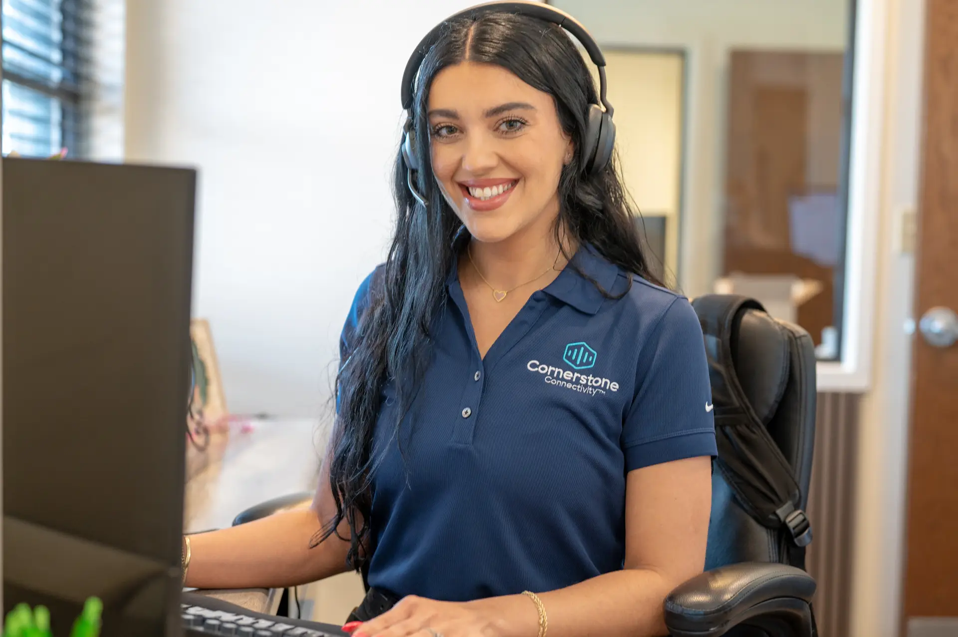 Customer service representative wearing a headset and smiling while working at a computer in an office.