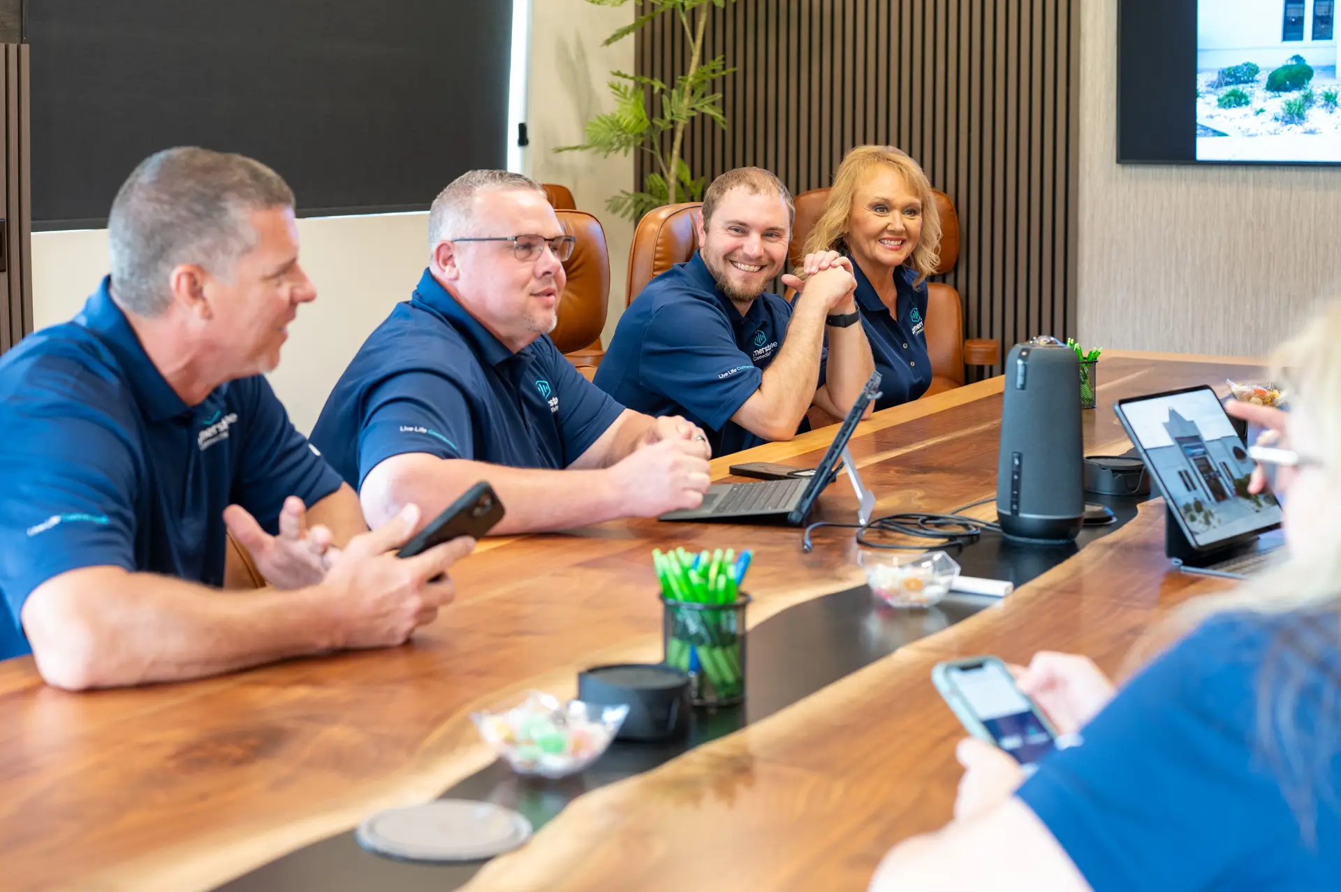 Team members in blue company polos sit around a conference table, smiling and collaborating during a meeting.