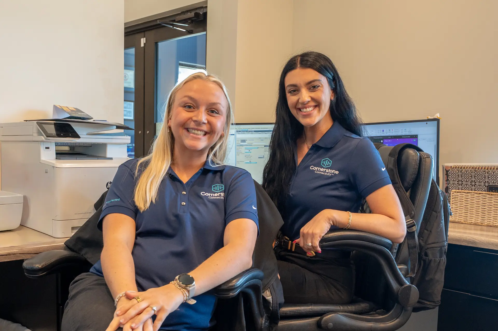 Smiling customer service representatives seated at a computer workstation.