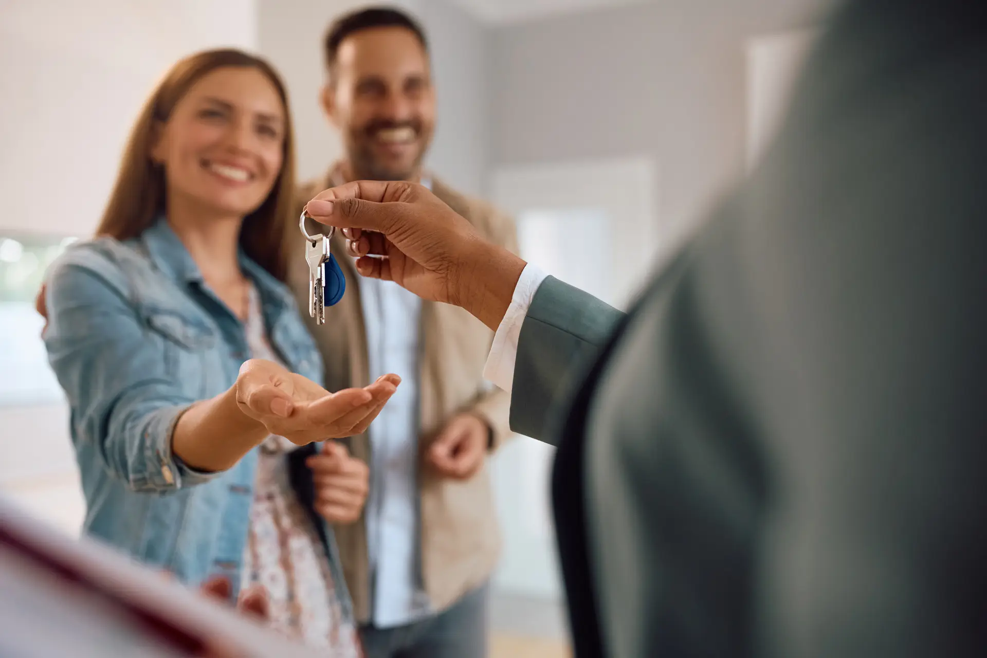 Real estate agent hands house keys to a smiling couple inside their new home.