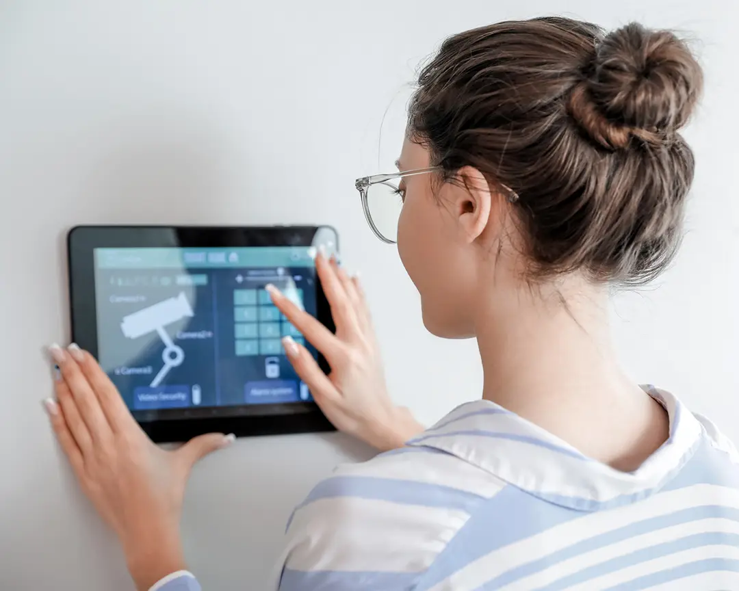 Person using a wall-mounted smart home security control panel with touchscreen camera and security system controls.
