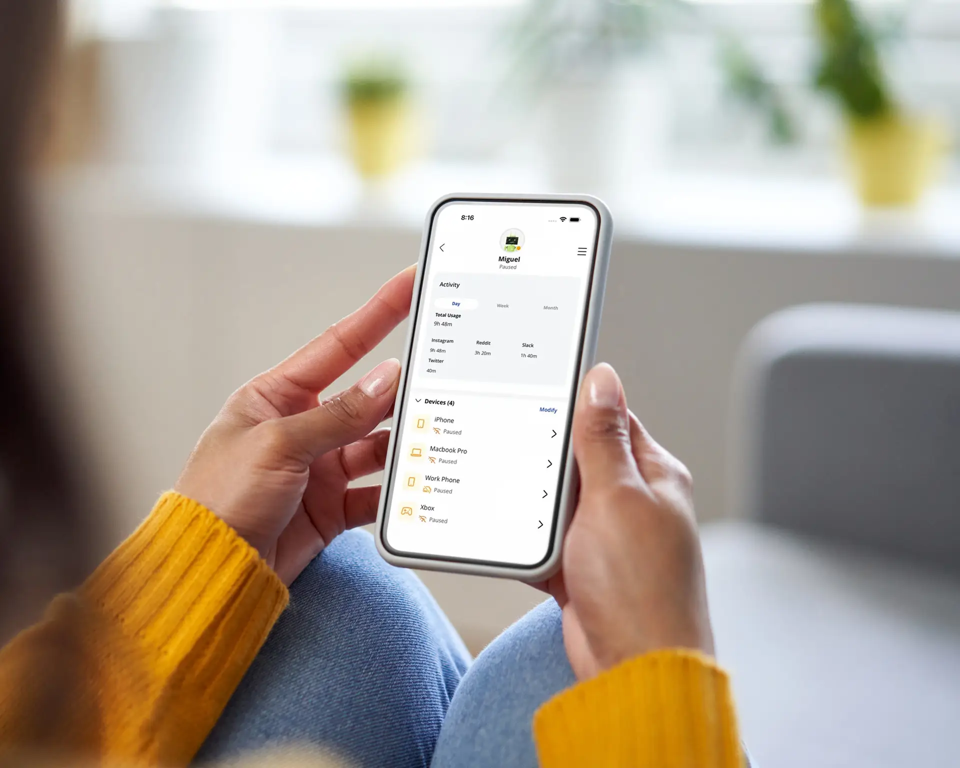 Person holding a smartphone displaying a parental controls app with device activity and usage settings.