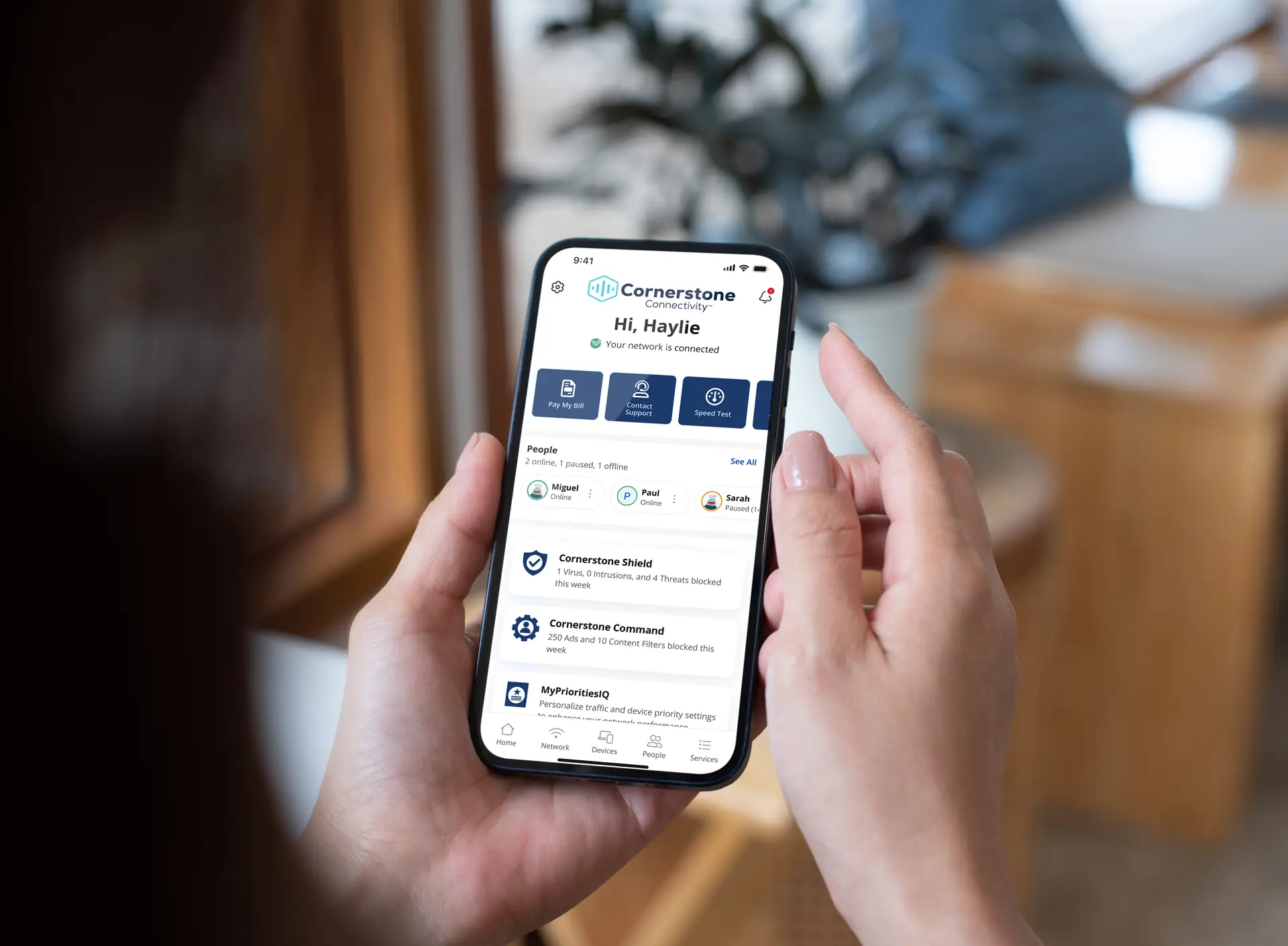Person holding a smartphone displaying the Cornerstone Connectivity app dashboard, showing network status, connected users, support options, and security features.