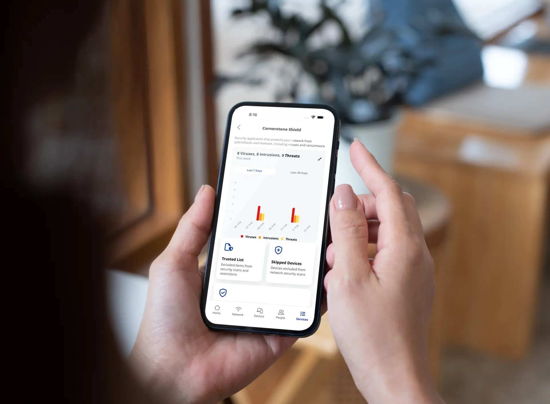 Person holding a smartphone displaying a network security app dashboard with threat monitoring and device protection activity.