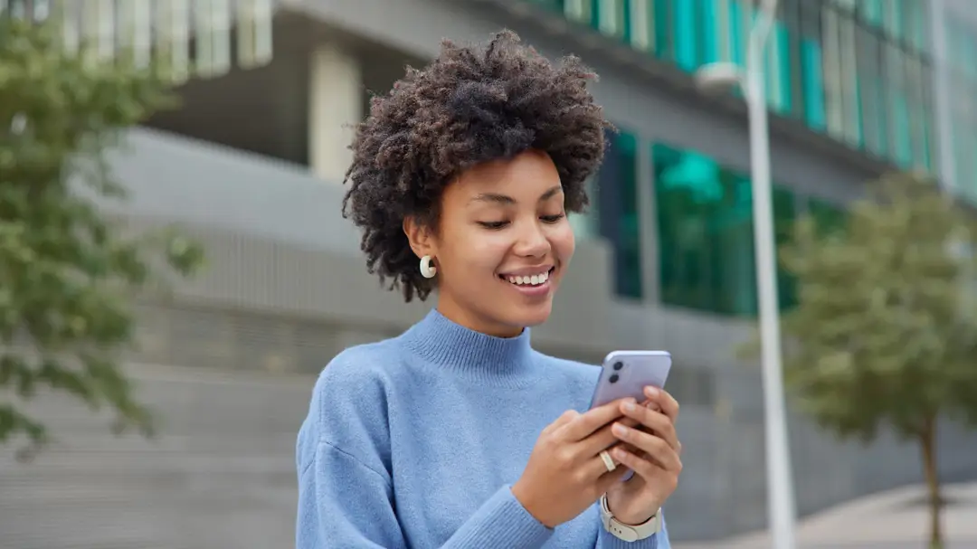 A smiling woma looking at her smartphone in an outdoor urban setting.