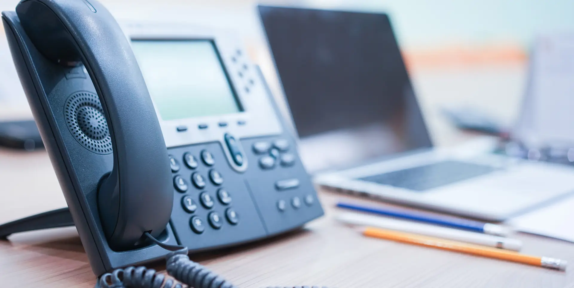 Office desk with a business phone, laptop, and office supplies in the background.